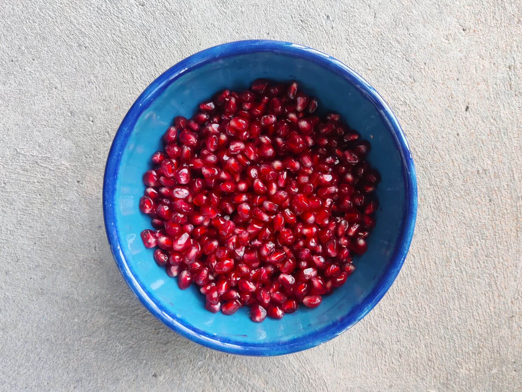 A blue bowl filled with seeded pomegranates