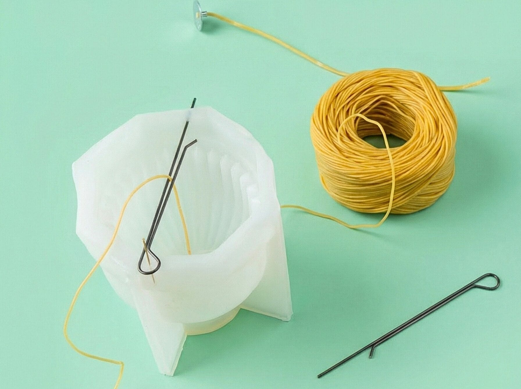 Centering a beeswax-coated cotton wick inside a silicone mold using a metal wick holder before pouring melted beeswax.