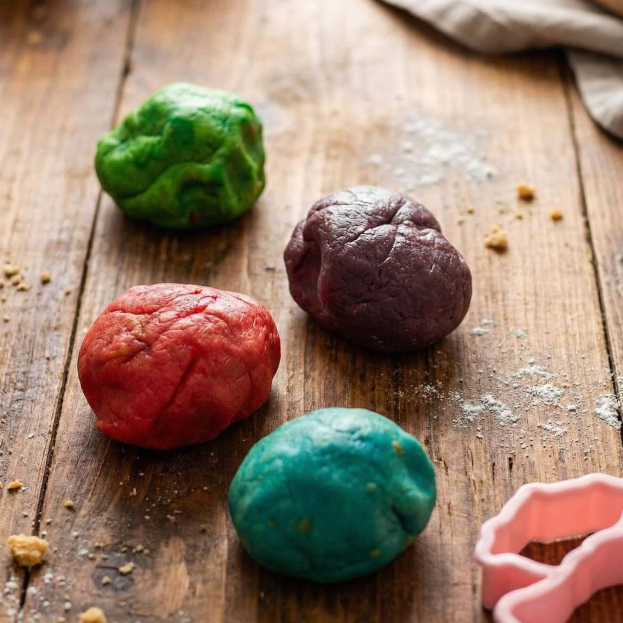 Portions of butter cookie dough coloured green, red, blue, and purple ready for rolling