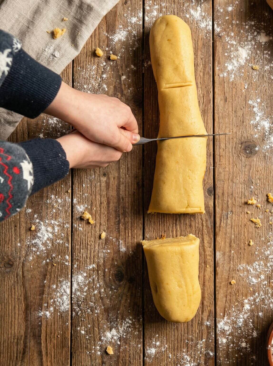 Cutting a rolled butter cookie dough sausage into portions on a floured wooden surface