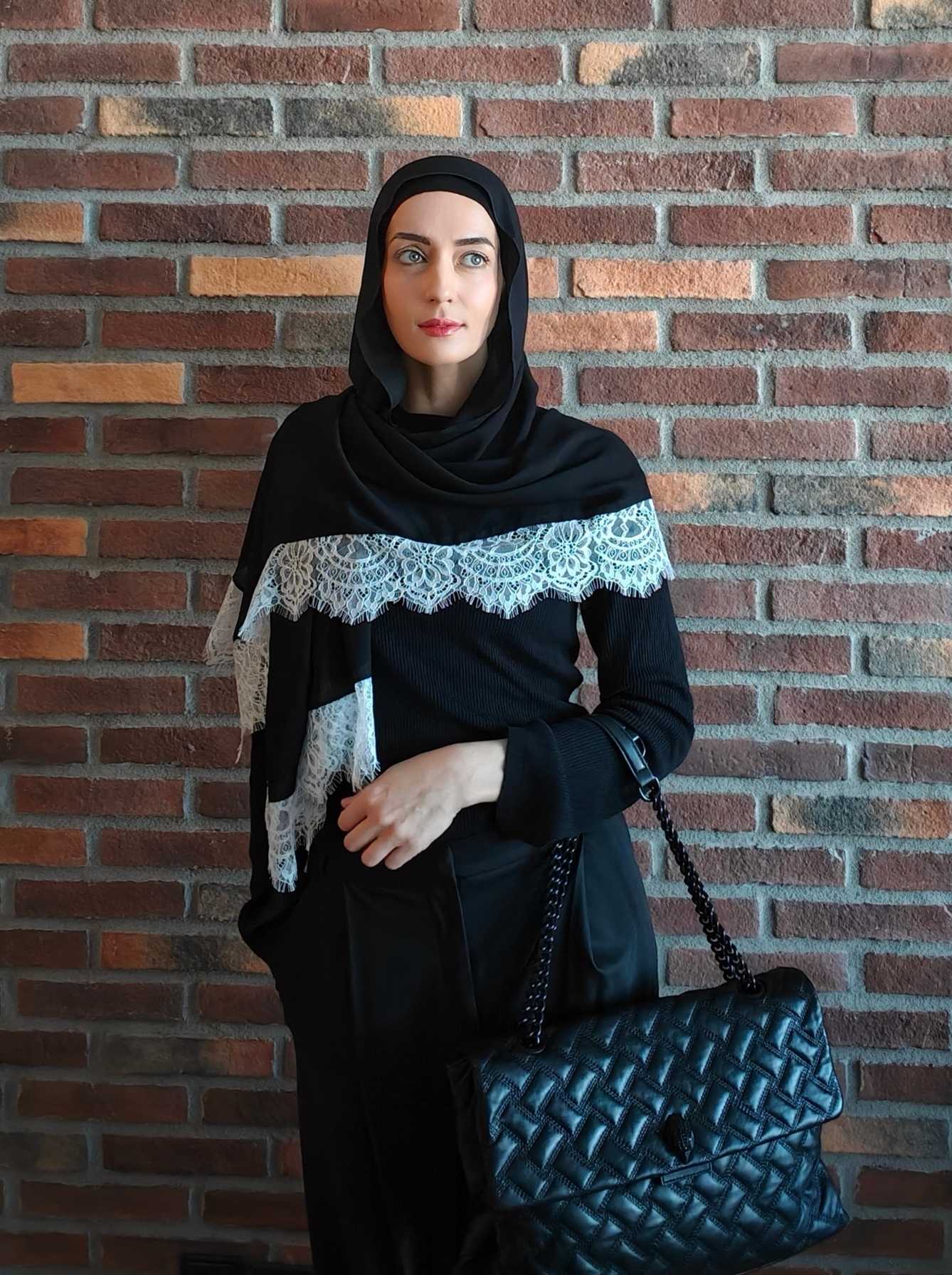 Woman styling a black lace hijab with an all-black tailored modest outfit