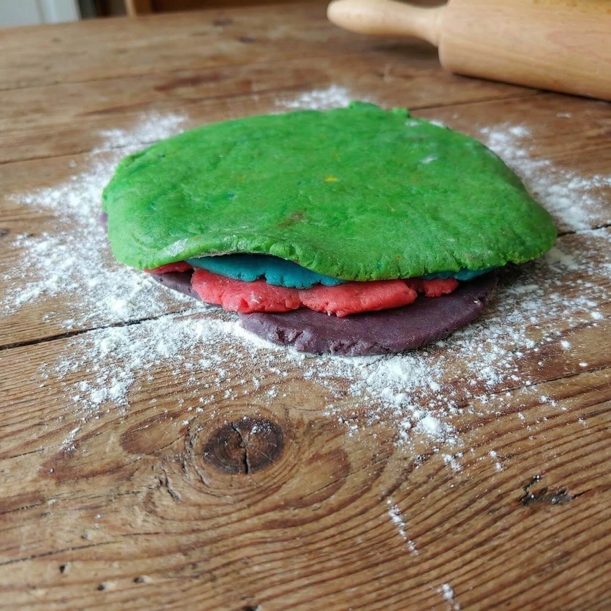 Stacked layers of coloured cookie dough pressed together on a floured wooden table