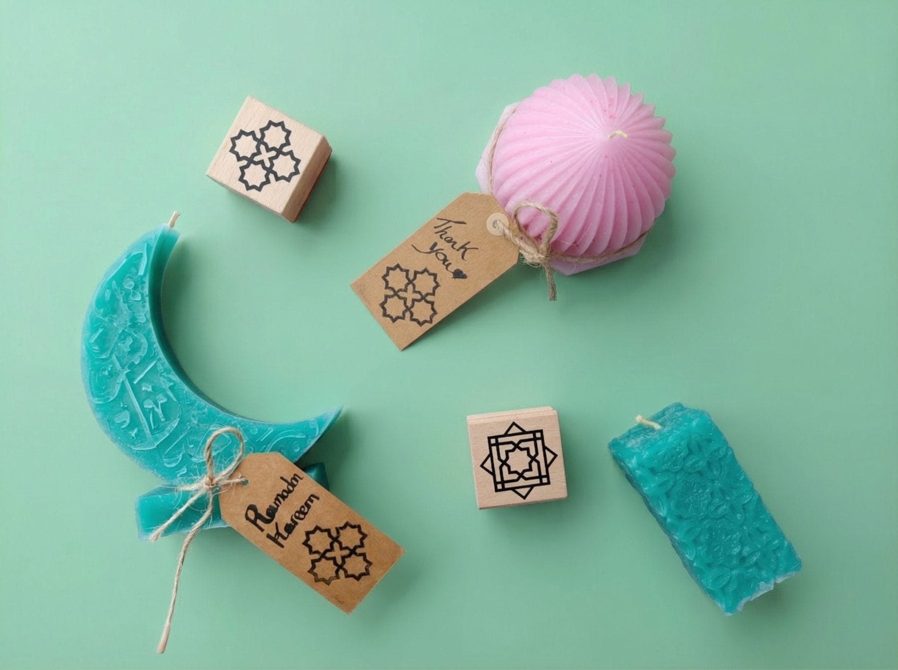 Pastel beeswax Ramadan candles styled with twine and kraft gift tags stamped with Islamic geometric patterns, alongside wooden stamp blocks.