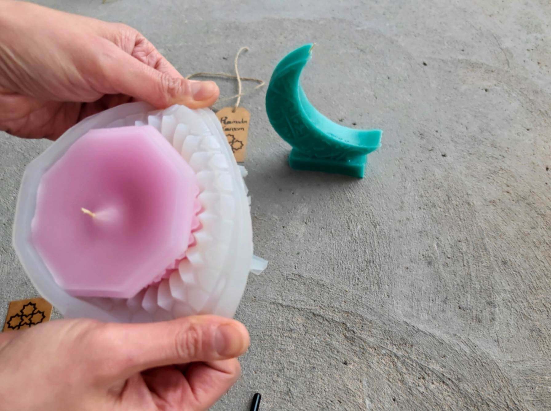 Peeling back a silicone mold to release a pastel pink beeswax candle, with a crescent candle in the background.