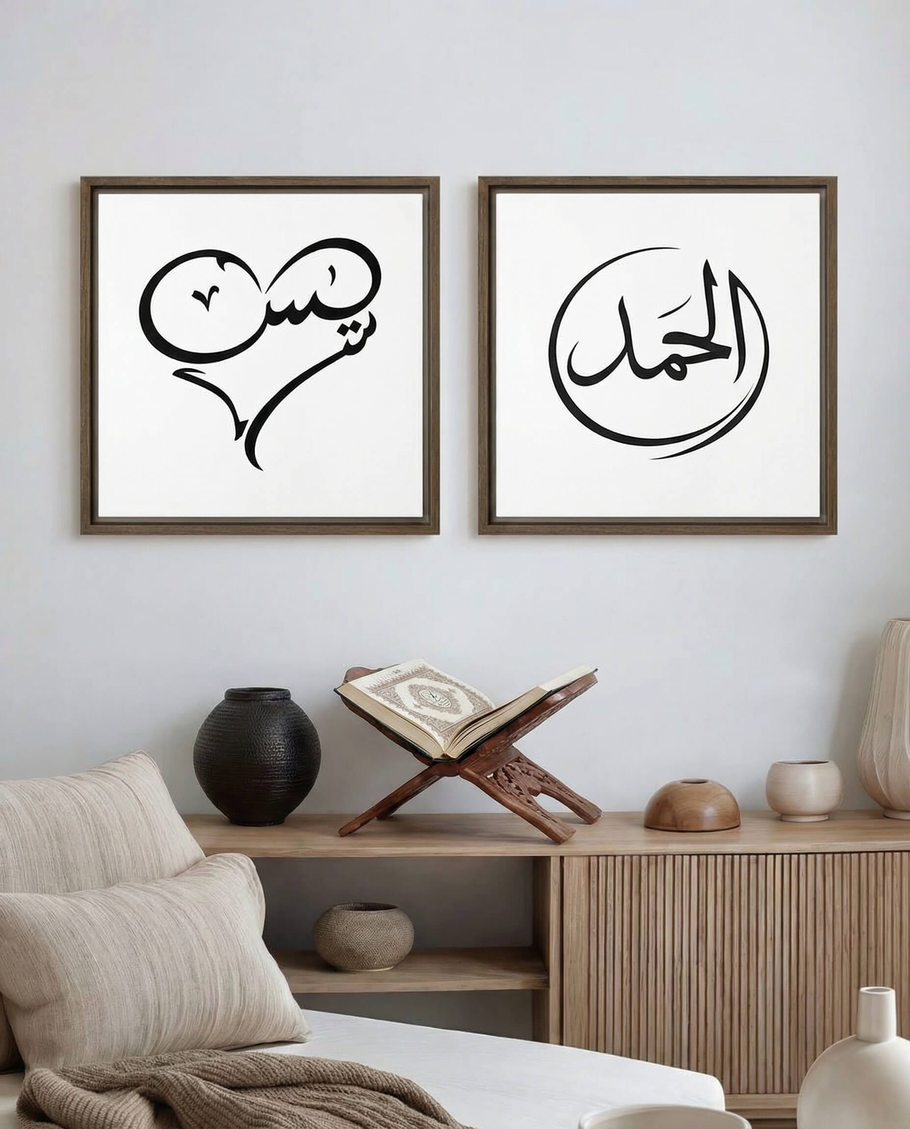Two framed minimalist black calligraphy artworks displayed side by side above a wooden sideboard: on the left, the word “Yasin” shaped into a heart; on the right, the word “Al-Hamd” enclosed within a circular form.